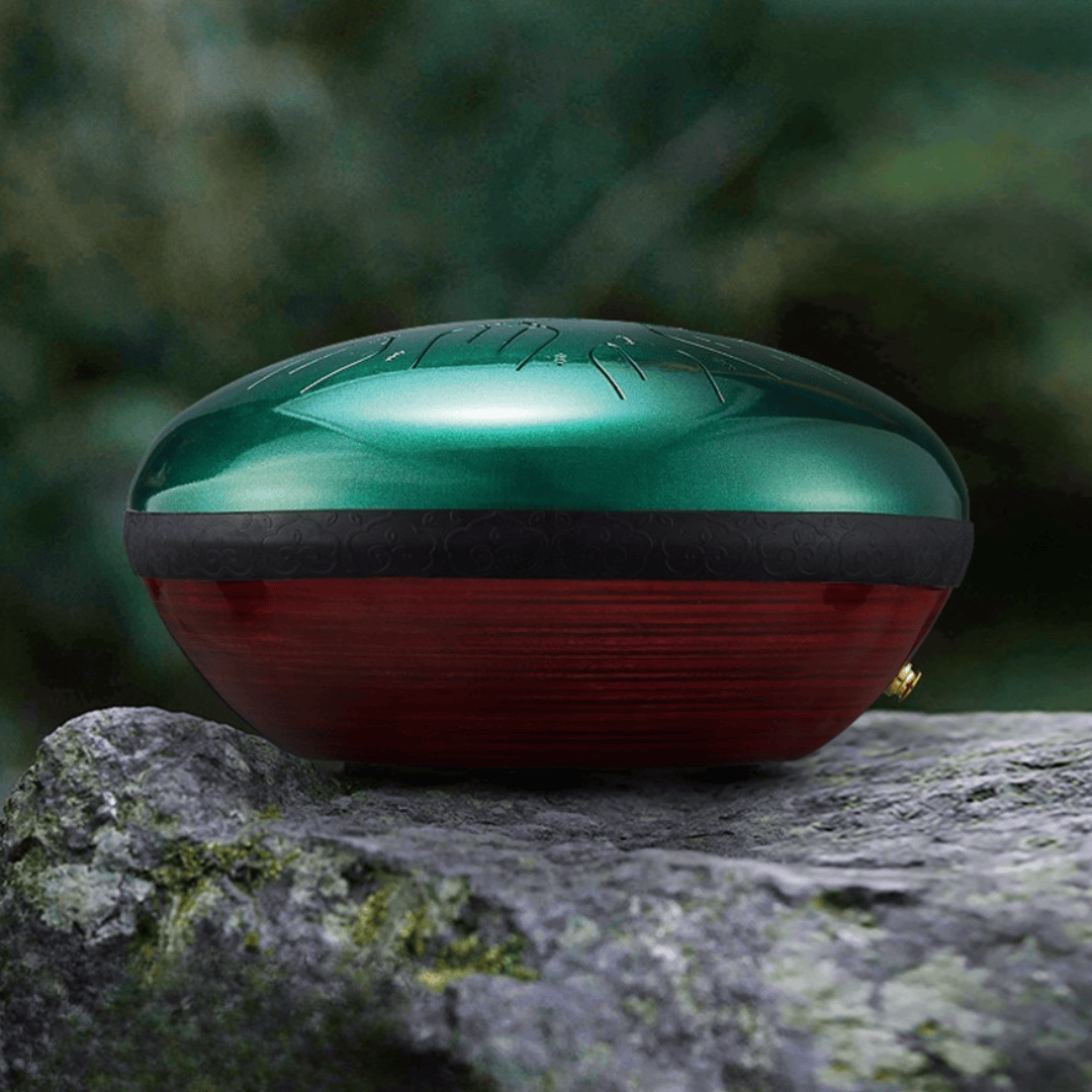 Side view of Hluru EQ Ethereal Tongue Drum placed on a rock, showing emerald steel top and red wooden body.