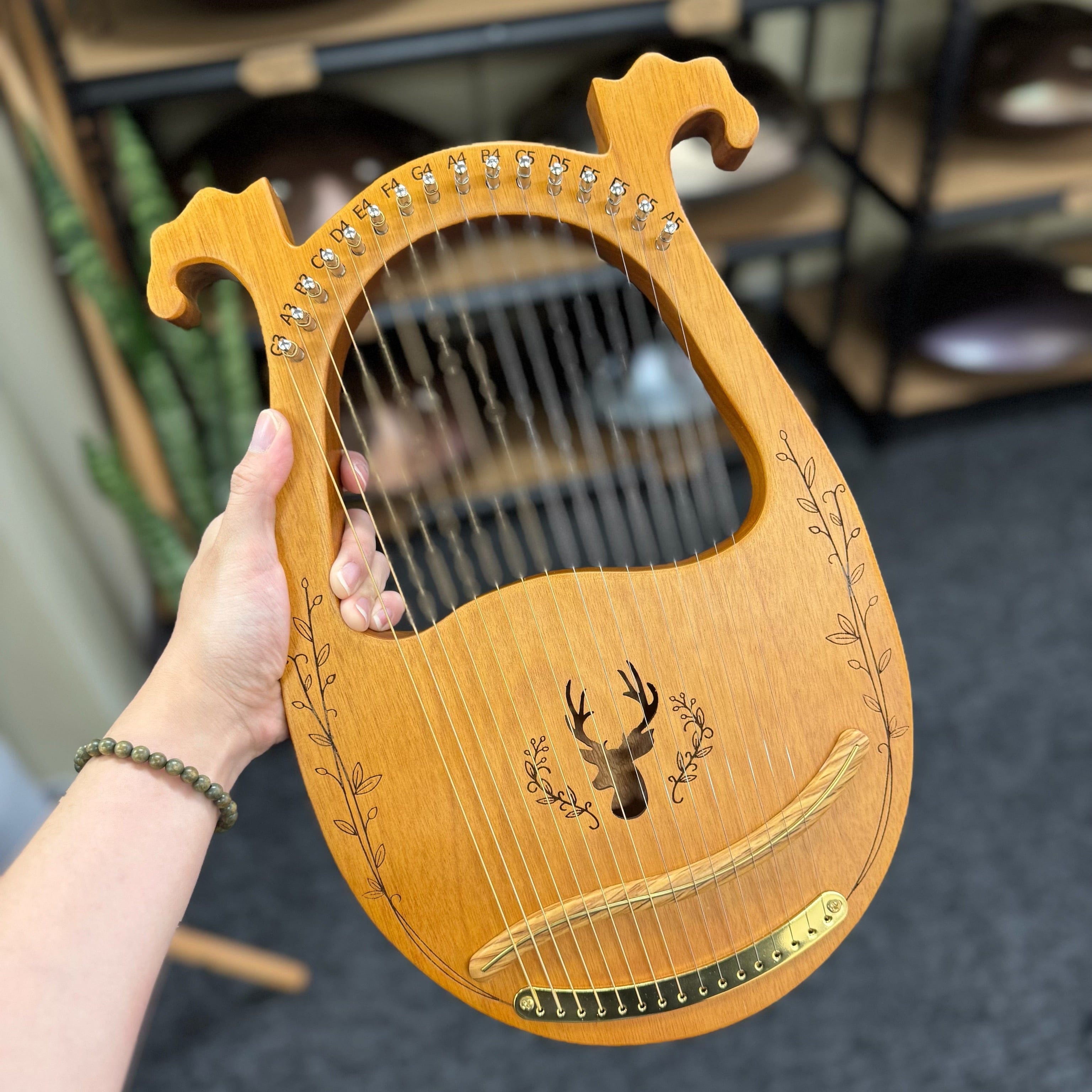 Wooden lyre with deer design held by a hand against a blurred indoor background